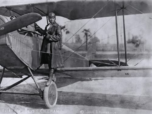 A woman stands on the wing of an airplane.