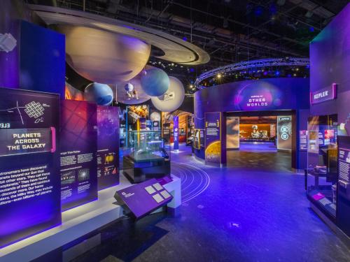 A view of the Kenneth C. Griffin Exploring the Planets Gallery. The overwhelming color of the gallery is purple. There is a model of a solar system hanging from the ceiling, with signage on the walls. 