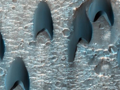 Arrowhead shaped dark splotches cover the cratered surface of Mars.