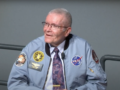 Fred Haise wearing a light blue NASA jacket embroidered with the Apollo 13 patch and a patch for "The Society of Experimental Test Pilots"