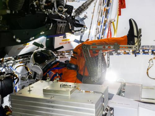 A mannequin wearing an orange spacesuit seated in a spacecraft.