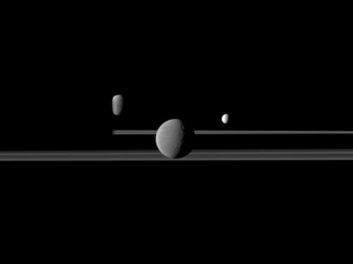 Three moons against a dark background. The moon in the middle appears to be the largest while the moons to the left and right are much smaller looking.