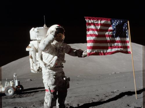 An astronaut stands on the surface of the Moon while touching the American flag