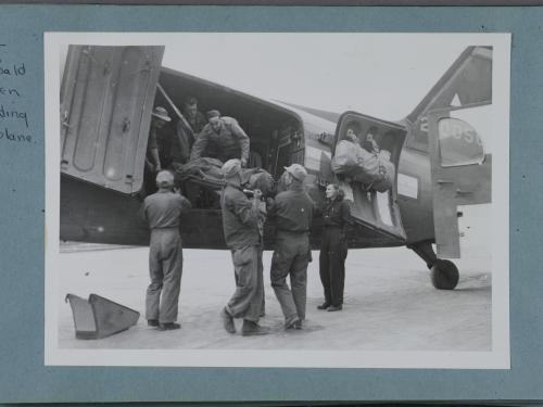 Black and white image of men and women in uniform offloading materials from a plane.