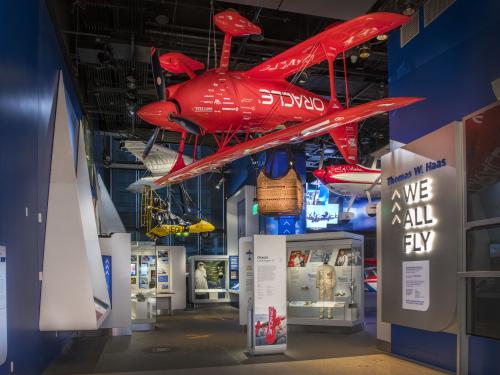 A bright red airplane hanging upside down in the entrance to an exhibition.