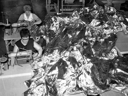 Black and white image of two women stitching together a parasol sunshade.