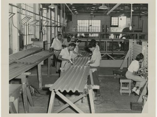 black and white photograph of men and women working on a large piece of corrugated metal