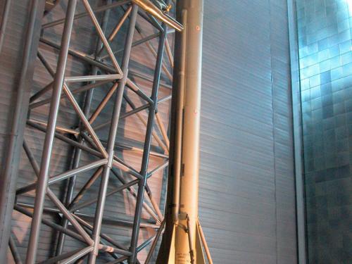 A large olive green rocket on display in a hangar with signage in front of it.