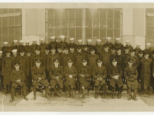  A partial view of a photograph of the entire crew of the USS Shenandoah in April 1924. A row of men sit posed in front of the camera with two rows of men standing behind them.