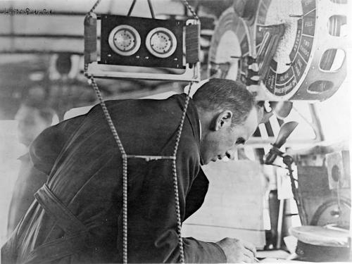 A man seen from the side, bent over a table with pencil in hand.