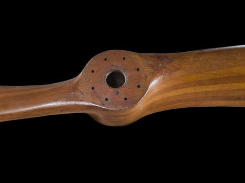 A wooden propeller is photographed against an all black backdrop.