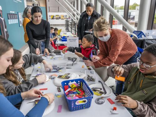 Young visitors sit at a table, decoration eclipse viewers, while assisted by adults. 