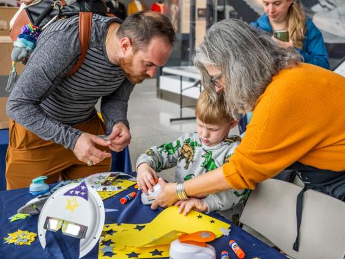 A young visitor constructs an eclipse viewer while helped by his guardians and museum staff. 