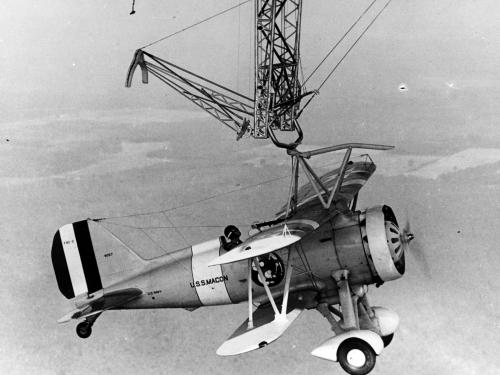 A small monoplane hangs from a hook high in the sky.