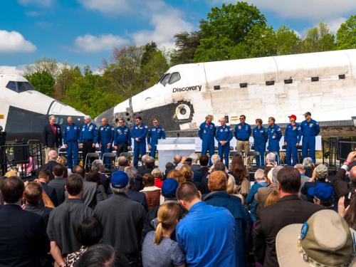 A group of astronauts stand next to two space shuttles that are nose to nose.