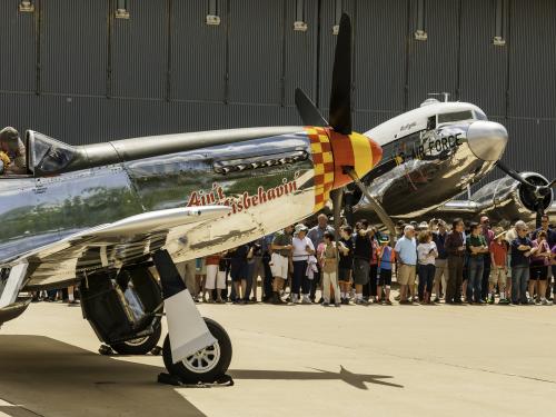 The noses of two World War II aircraft gleam in the sun as a line of visitors waits to explore them on the tarmac outside the Steven F.  Udvar-Hazy Center.