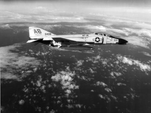 Black and white photo of a military aircraft flying, with clouds all around it 