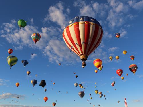 Colorful hot air balloons fill a bright blue sky.