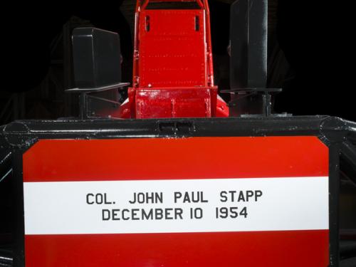 Straight metal seat attached to the middle of a rocket sled. Col. John Paul Stapp December 10 1954 is painted on the seat. 