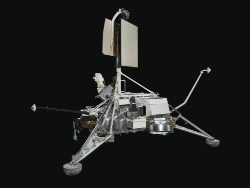 Metal lunar lander with three triangular space frame legs connected to central body with panels hanging in museum.