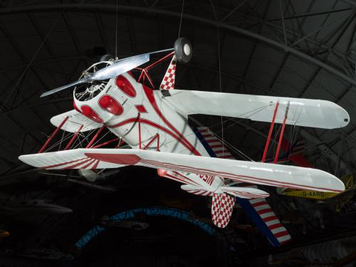 White and red painted single-engine aerobatic and military trainer biplane hanging in the museum.