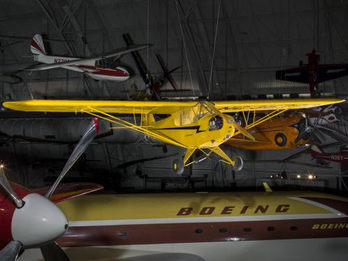 Yellow monoplane hanging in the museum with other planes in view