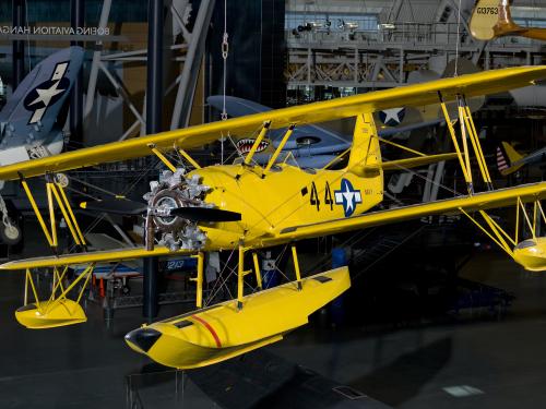 Bright yellow bi-plane with hand crank start hanging in the Steven F. Udvar-Hazy Center.