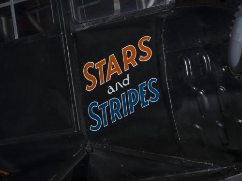 The words Stars and Stripes are painted orange and blue on the side of an airplane. 		