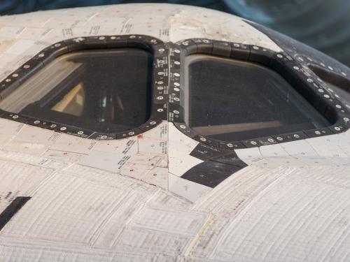 A close-up view of the cockpit windows of a space shuttle, highlighting the thermal protection tiles around the windows designed to withstand extreme temperatures during re-entry into Earth’s atmosphere.