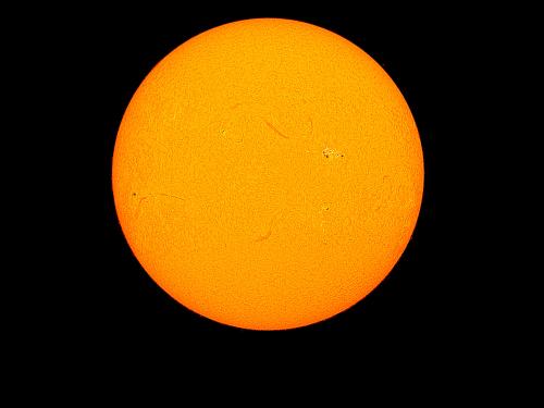 Disk view of the Sun's chromosphere. A few filaments, or darker lines of gases floating away from the chromosphere, are visible. A sunspot cluster (two dark spots) surrounded by a lighter-colored phage cloud is visible in the upper right quadrant.