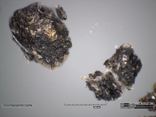 Microscopic view of black particles extracted from adhesive on a World War II era aircraft. The particles are mostly black but have some light discoloration to them.