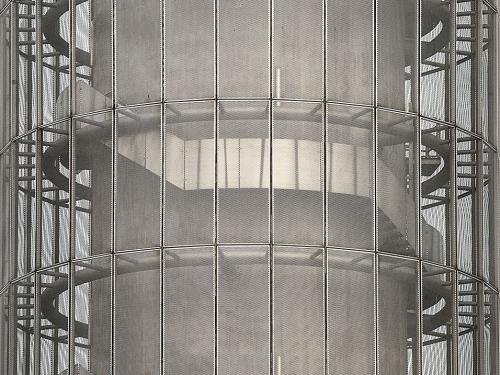 Partial view of the base of the air traffic control tower at Bangkok-Suvarnabhumi Airport. The base features a cylinder interior that looks almost like spiral stairs. The cylinder is protected by another cylinder made from metal bars and mesh.