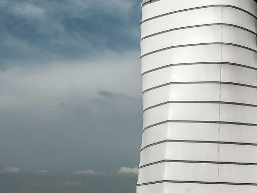 Partial view of the base of the air traffic control tower at Vienna International Airport. The base features a white, concrete structure with four sides that jut out into eight sides in the higher section.