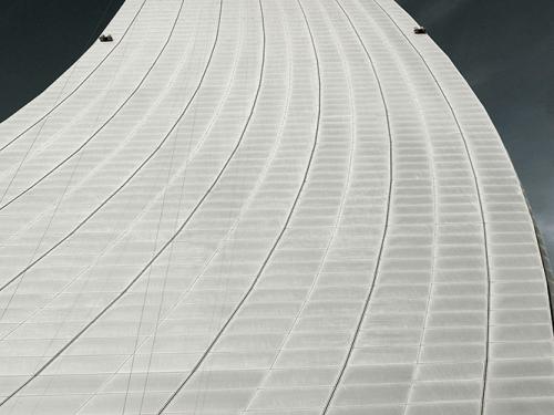 Partial view of the air traffic control tower at Abu Dhabi International Airport. The base has a curved, white tile pattern with the top leading to a metal control tower base.