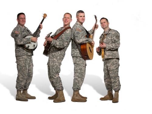 A group of four men in Army uniform pose informally with their instruments. The person on the far left is playing a banjo while everyone else seems to be playing guitar.