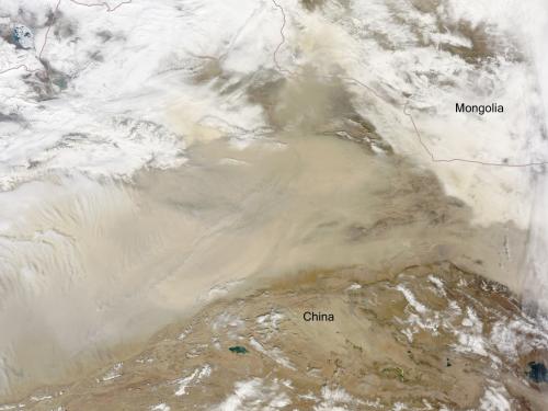 Satellite view of a desert near the border of China and Mongolia. The view is partially obscured by clouds on the top and bottom of the view as well as a dust storm in the center.