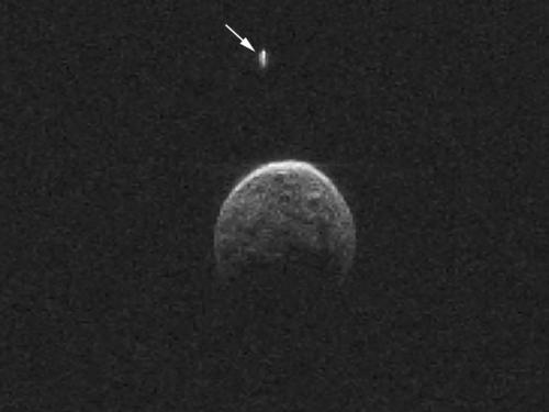 Radar image of an asteroid during its nearest approach to Earth. The asteroid's singular moon is pointed out using a white arrow.