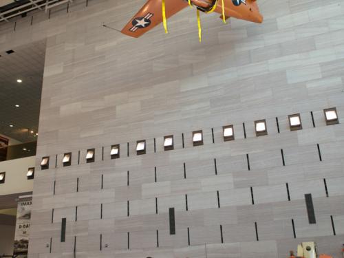 Several Museum employees stand under an orange monoplane hanging on the ceiling of the Museum's Boeing Milestones of Flight Hall. Nearby, an orange machine used to lift employees toward the aircraft is stationary.