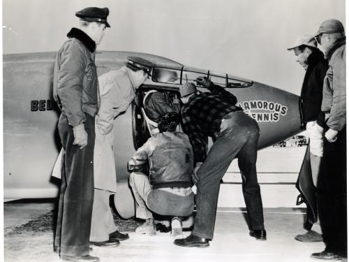 Chuck Yeager, a pilot, prepares for a flight in the cockpit of the Bell X-1 monoplane. Multiple people assist him prior to takeoff.