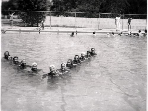 A group of female pilots in training during World War II swim together in a triangle formation in a pool.