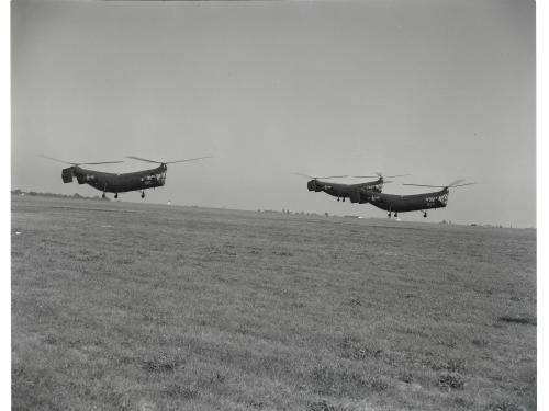 Three helicopters with two sets of propellors apiece vertically fly together during an airshow.