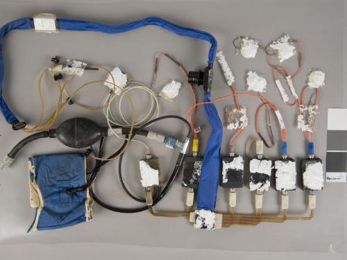 A during-conservation view of an blue Apollo program medical instrumentation harness. Majority of the harness and various parts have been removed from its previous white board.