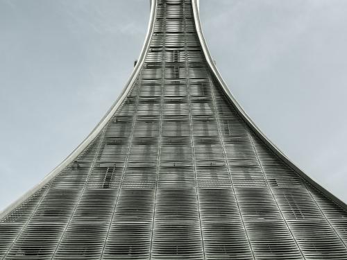 Air traffic control tower with a vial-shaped support structure that expands at the bottom from a narrow top. The support structure looks to be made from sections of steel.