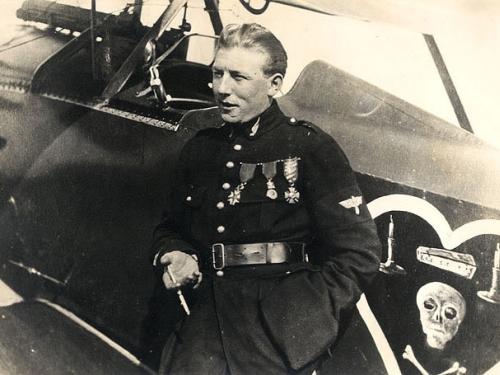 Charles Nungesser, a French World War I male pilot, poses in front of his aircraft and next to his famous insignia on the aircraft. The insignia consists of a skull, crossbones, coffin, and two candles inside a heart.