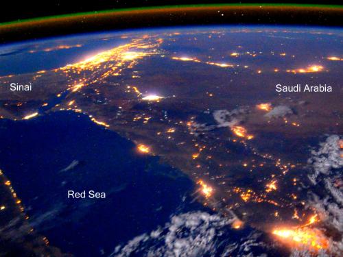 A partial satellite-style view of the Earth, with a focus on North Africa and the Middle East at night. Lights can be seen throughout heavily populated areas.