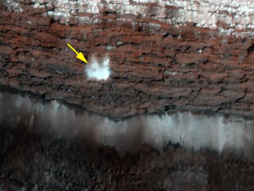 A frost-covered cliff on the northern polar surface of Mars. A yellow arrow points out potential frost that is in the process of freefalling.