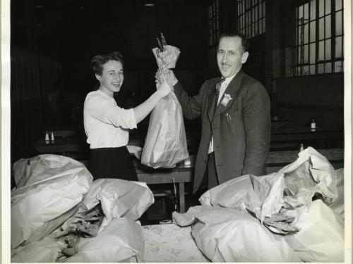 Two employees of an aeronautical corporation in the 1940s smile as one employee hands a turkey to the other employee.