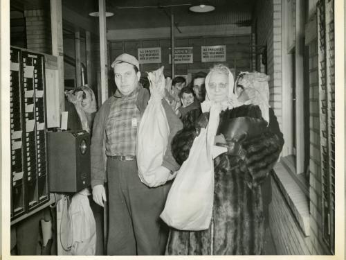 Multiple employees of an aeronautical corporation in the 1940s hold their bagged turkeys.