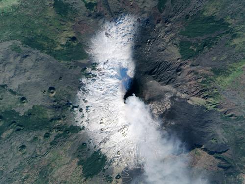 Satellite view of Mount Etna, a volcano in Italy, that is in the process of erupting. Ashes and gases are seen as a set of white clouds above the eruption site.