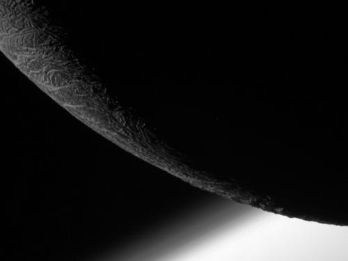 Partial view of the mostly non-illuminated Enceladus, a moon of Saturn.